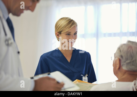 Doctor and nurse talking to older patient in hospital room Stock Photo