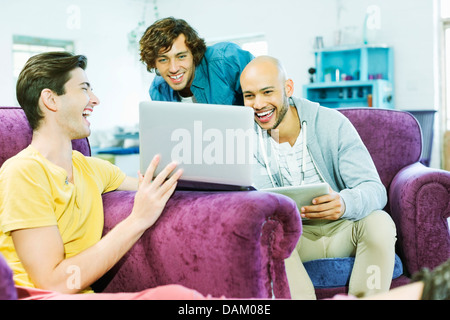 Men using laptop together in living room Stock Photo