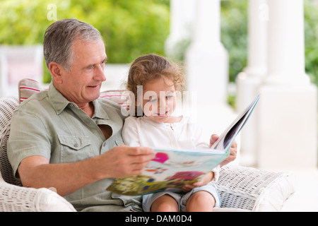 Older man reading to granddaughter on porch Stock Photo