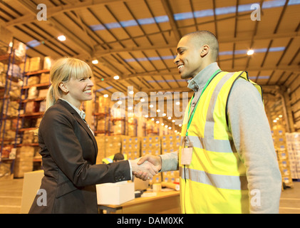 Businesswoman and worker shaking hands in warehouse Stock Photo