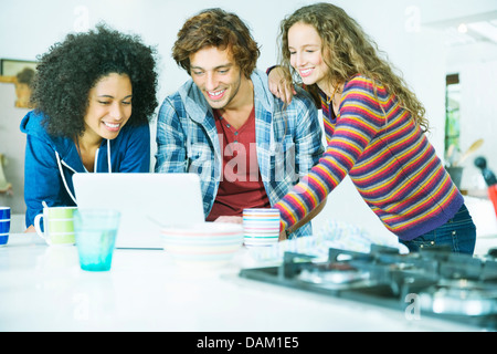 Friends using laptop together in kitchen Stock Photo