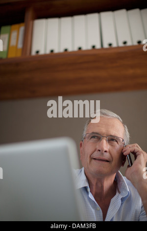 Older man talking on cell phone at desk Stock Photo