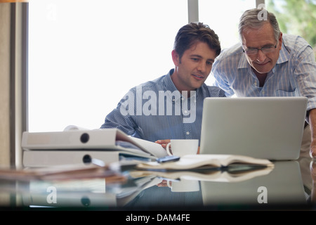 Older man and younger man working together at desk Stock Photo