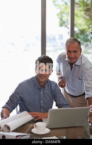 Older man and younger man working together at desk Stock Photo