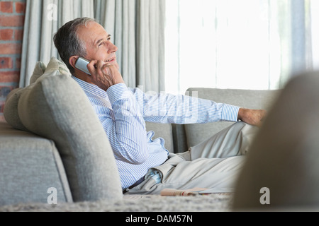 Older man talking on cell phone on sofa Stock Photo