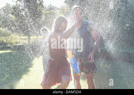 Couple playing in sprinkler in backyard