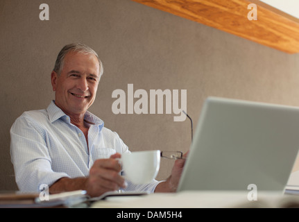 Older man having cup of coffee at desk Stock Photo