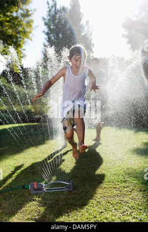 Boy playing in sprinkler in backyard Stock Photo