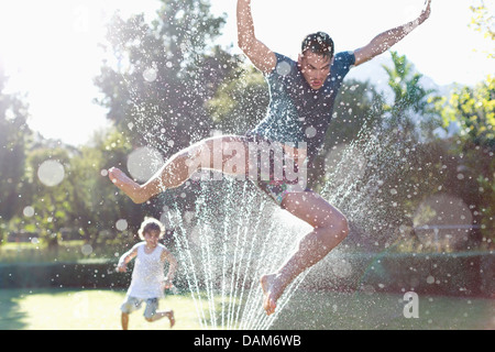 Father and son playing in sprinkler in backyard Stock Photo
