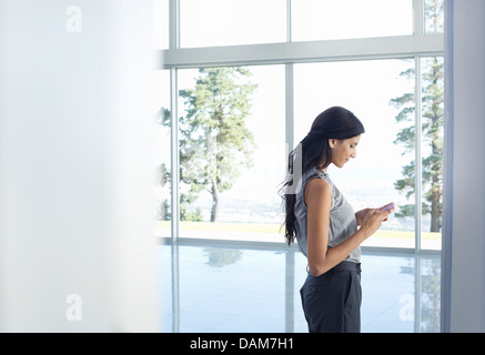 Businesswoman using cell phone at window Stock Photo
