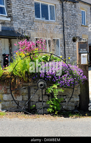 old wagon wheel on a stone wall surrounded by flowers Castleton Derbyshire England uk Stock Photo