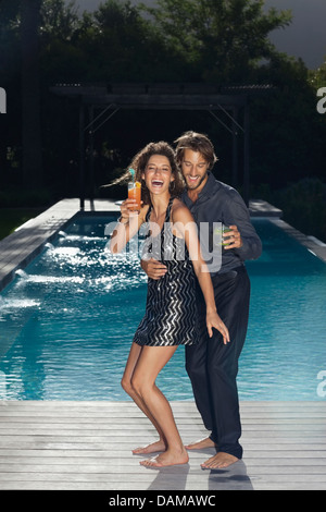 Couple having drinks by swimming pool Stock Photo