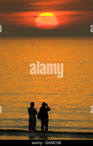 two strollers standing at the beach and watching the sunset, Belgium Stock Photo