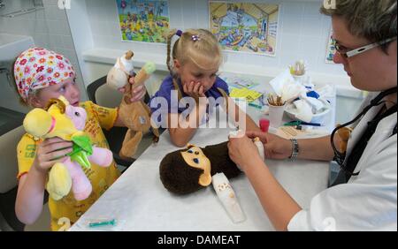 A student of medicine (r) examines the health condition of a stuffed animal in Halle(Saale, Germany, 6 June 2011. Students of the university hospital have for the sixth time now opened a teddybear hospital. In the next five days, children can come with their stuffed animals to mend open seams, broken arms and missing eyes. The project wants to make children less scared of the docto Stock Photo