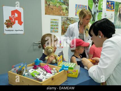 A student of medicine (r) examines the health condition of a stuffed animal in Halle(Saale, Germany, 6 June 2011. Students of the university hospital have for the sixth time now opened a teddybear hospital. In the next five days, children can come with their stuffed animals to mend open seams, broken arms and missing eyes. The project wants to make children less scared of the docto Stock Photo