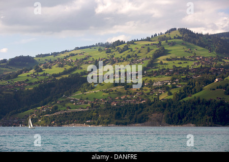 white sail boat on Lake Thunersee, Switzerland with traditional swiss chalets on the mountainside Stock Photo