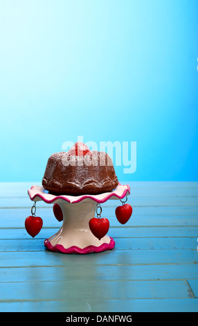 Chocolate mini pound (bundt) cake with strawberry on top and icing sugar on antic stand with red hearts on rustic table Stock Photo