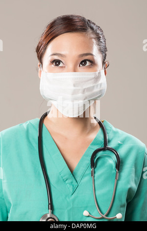 Chinese doctor wearing a face mask, green scrubs and stethoscope. Looking upwards. Stock Photo
