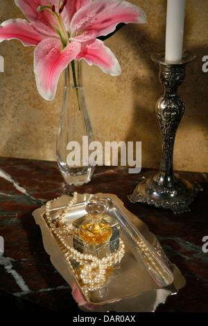 feminine still life, tabletop w/ perfume bottle, pearls on silver tray w/ candle and flower Stock Photo