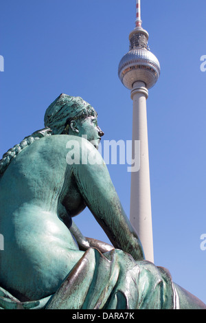 One of the statues in the Neptunbrunnen ensemble with the Fernsehturm (TV Tower) in background Mitte Berlin Germany Stock Photo