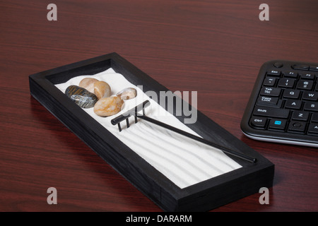 A miniature Zen garden on a desk beside a computer keyboard Stock Photo