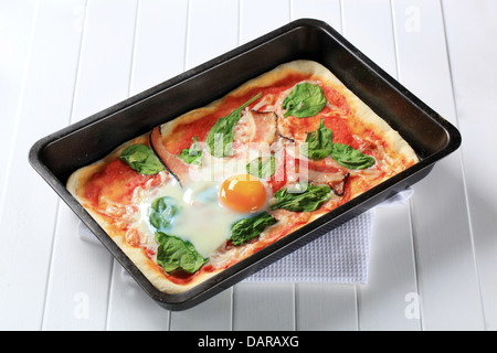 Pizza with prosciutto, spinach leaves and oven-roasted egg on top Stock Photo