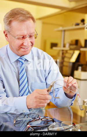 Elderly optician repairing glasses with bending pliers Stock Photo