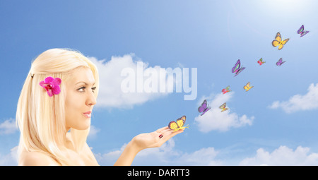 Beautiful blond female with many butterflies on her hand, against cloudy sky Stock Photo