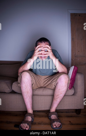 man covering face watching tv or television in fear Stock Photo