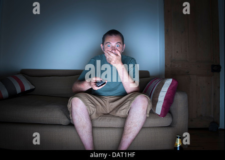 man covering mouth watching tv or television in disbelief Stock Photo