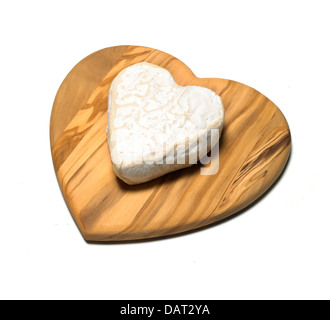 heart shape piece of cheese on a heart shaped wooden board cut out onto a white background Stock Photo