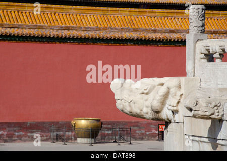 China, Beijing, Forbidden City. Carved dragon head with giant bronze urn that held water for extinguishing fire in the distance. Stock Photo