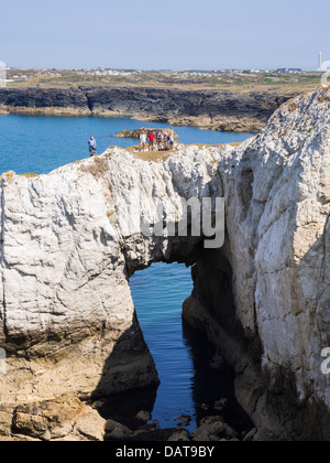 Ramblers on Bwa Gwyn or White Arch natural quartzite rock formation on Isle of Anglesey Coastal Path on seacliffs Rhoscolyn Anglesey Wales Stock Photo