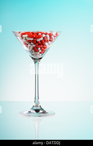 Red and white drug pills in the cocktail glass as a concept of drinking too much to have need for medicine Stock Photo