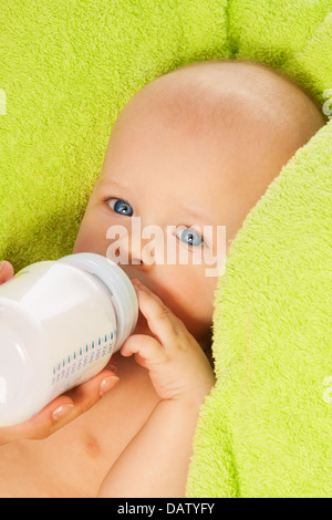 Little baby drink from bottle with milk laying on green towel Stock Photo