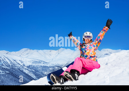 Happy excited woman in pink sit on snow holding snowboard with lifted hands Stock Photo