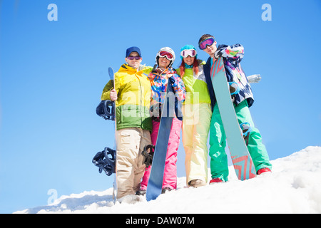 Four happy friends hug and hold snowboards standing in snow in winter Stock Photo