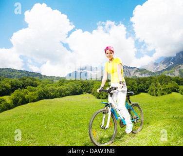 Happy young woman in bright clothes with red hair riding a bike Stock Photo