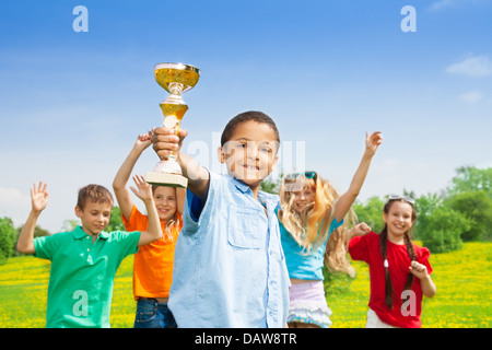 Portrait of black happy smiling little boy holding prize cup with his team on background Stock Photo