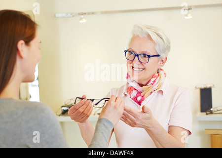 Senior optician giving new glasses to female customer
