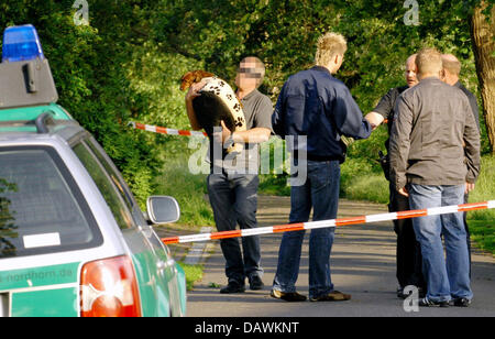 A policeman carries a dog (L) next to other policemen behind a barrier tape surrounding a detached house and its garden in Ringe, Germany, 20 May 2007. The corpses of a 52 year old man, his 54 year old wife and the man's 75 year old mother were found in the house (wife and mother) and in the garden (man) on Saturday, 19 May 2007. Photo: Werner Westdoerp Stock Photo