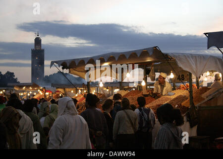 A market shop selling nuts, dates and other sweets and crowds of locals and tourists shown on Djamaa el-Fna square at dusk in Moroccon royal city Marrakech, Morocco, 7 April 2007. The famous Kutubiya mosque can be seen in the background. Its snake charmers, story tellers and cookshops attract masses of tourists and  day by day. Photo: Marijan Murat Stock Photo
