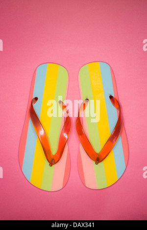 Flat lay shot of a pair of multicoloured flip flops on a pink background. Stock Photo