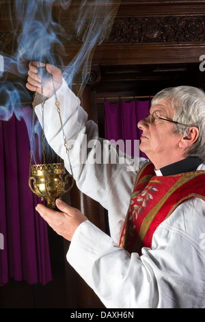 Priest in red chasuble burning incense during mass Stock Photo