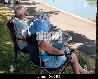 Old couple sat in the shade of a tree reading newspapers, Kingsbridge, Devon, UK 2013 Stock Photo