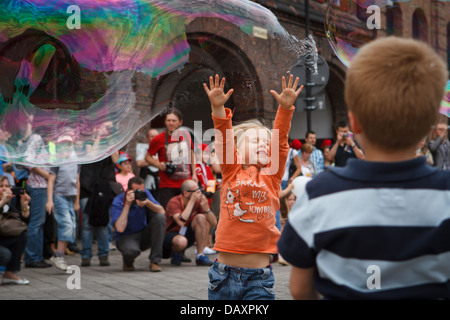 A girl catching big soap bubble during 'Industriada' 2013 street performance at Nikiszowiec main square. Katowice, Poland. Stock Photo