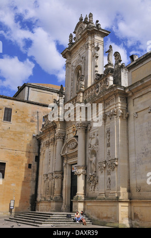 A couple sitting on the steps of Basilica di Santa Croce Lecce, Puglia, Italy, showing  its baroque facade