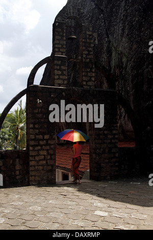 WOMAN & MULTI-COLOURED UMBRELLA ALUVIHARA ROCK CAVE TEMPLE MATALE SRI LANKA 11 March 2013 Stock Photo