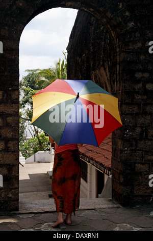 WOMAN & MULTI-COLOURED UMBRELLA ALUVIHARA ROCK CAVE TEMPLE MATALE SRI LANKA 11 March 2013 Stock Photo