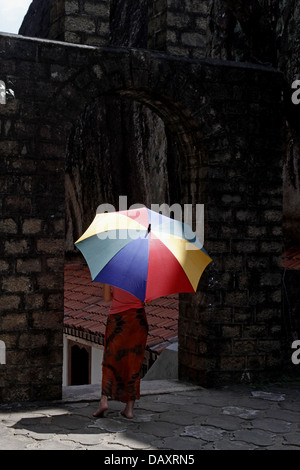 WOMAN & MULTI-COLOURED UMBRELLA ALUVIHARA ROCK CAVE TEMPLE MATALE SRI LANKA 11 March 2013 Stock Photo